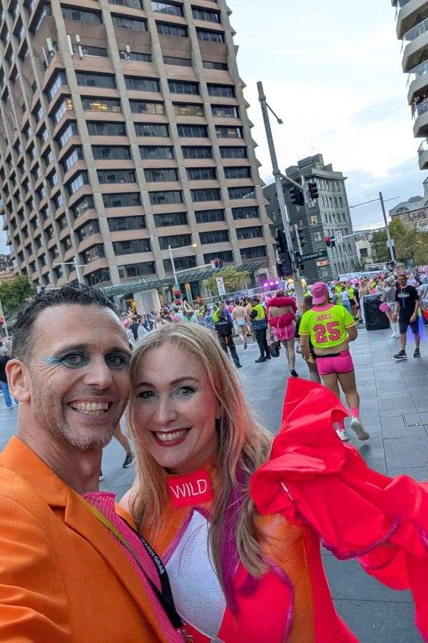 Selfie in the crowd on a Sydney street. Both are smiling, dressed in bright orange and pink, with glitter eye make-up.